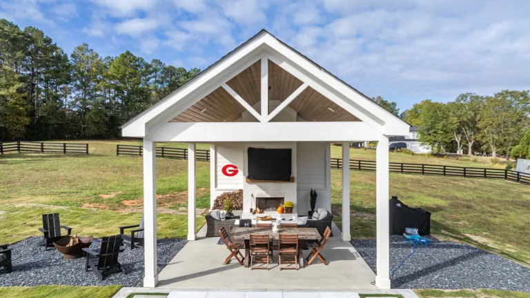A white pavilion with a table and chairs underneath it in a field.