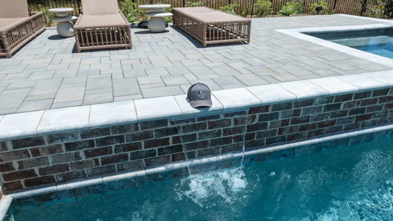 Poolside lounge chairs beside a raised brick spa with water spilling into the pool