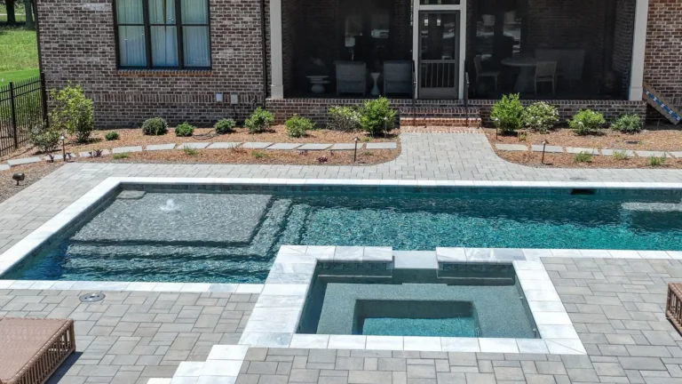 Backyard pool with a square hot tub and tiled coping beside a brick patio and house façade