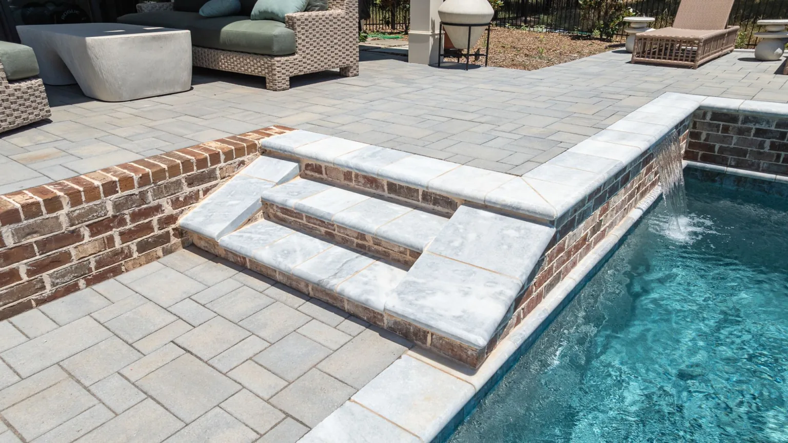 Poolside stone steps and deck beside a swimming pool with outdoor seating.