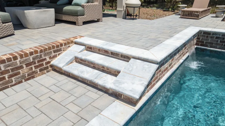 Poolside stone steps and deck beside a swimming pool with outdoor seating.