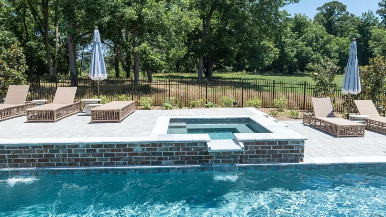 Backyard pool with a raised hot tub, lounge chairs, and umbrellas beside a wooded landscape