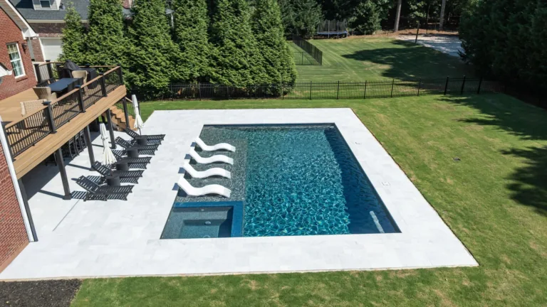 Backyard swimming pool with white deck, lawn, and deck chairs beside a house