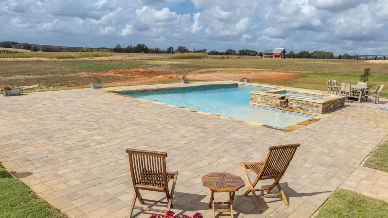 A patio with chairs and a table next to a swimming pool.