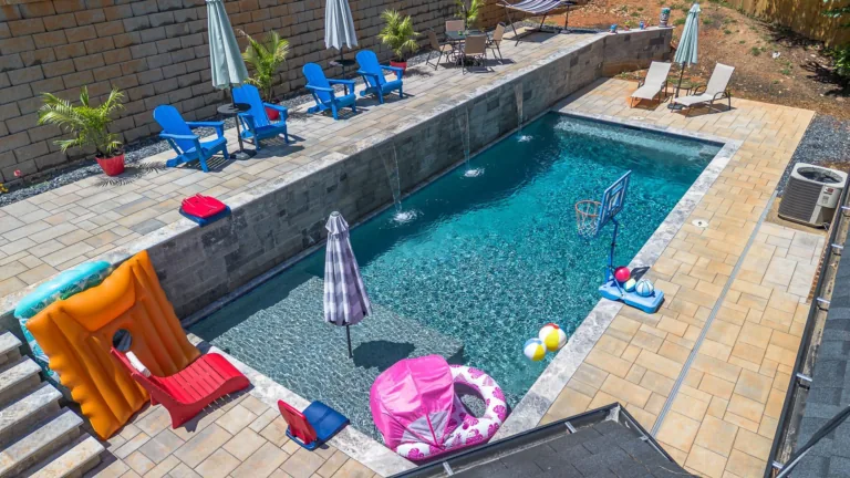 Backyard pool with lounge chairs, umbrellas, and pool toys.