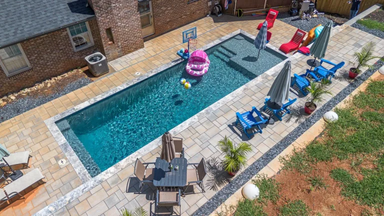 Overhead view of a rectangular pool with lounge chairs, umbrellas, and a dining area; red and blue inflatables are present.