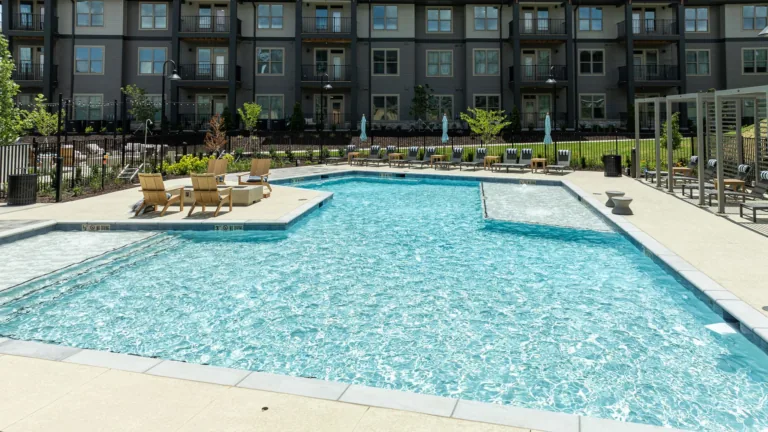 Outdoor apartment pool with turquoise water, lounge chairs, and surrounding modern buildings