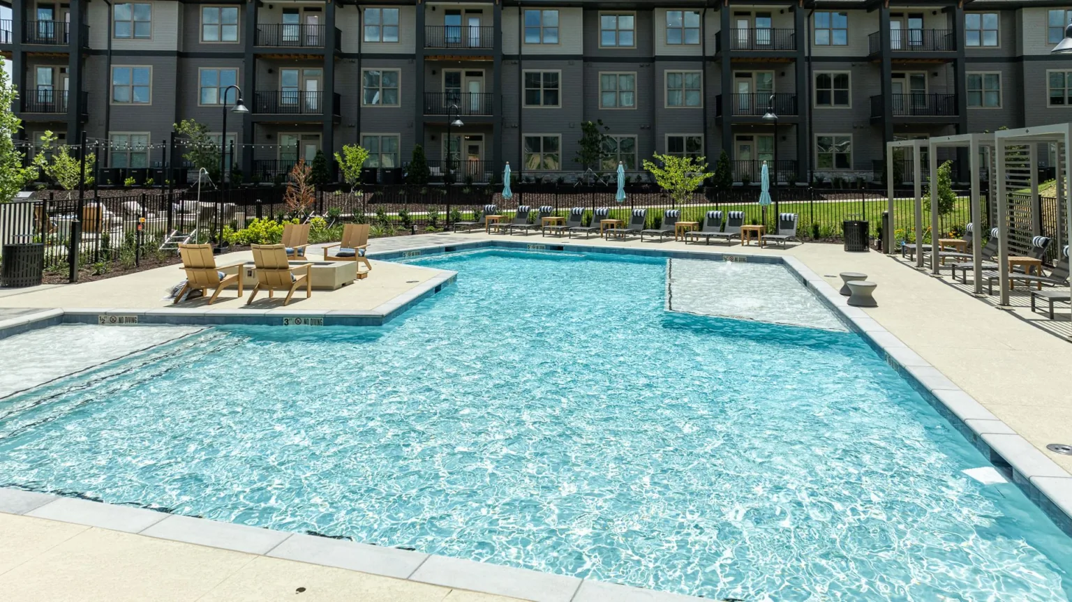 Outdoor apartment pool with turquoise water, lounge chairs, and a modern building courtyard backdrop