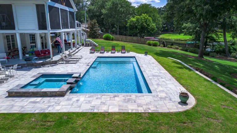Outdoor pool and spa next to a large house on a grassy hillside.