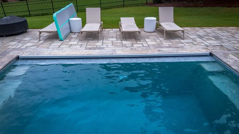 A pool with blue water, lounge chairs, and an inflatable mat on a stone patio.