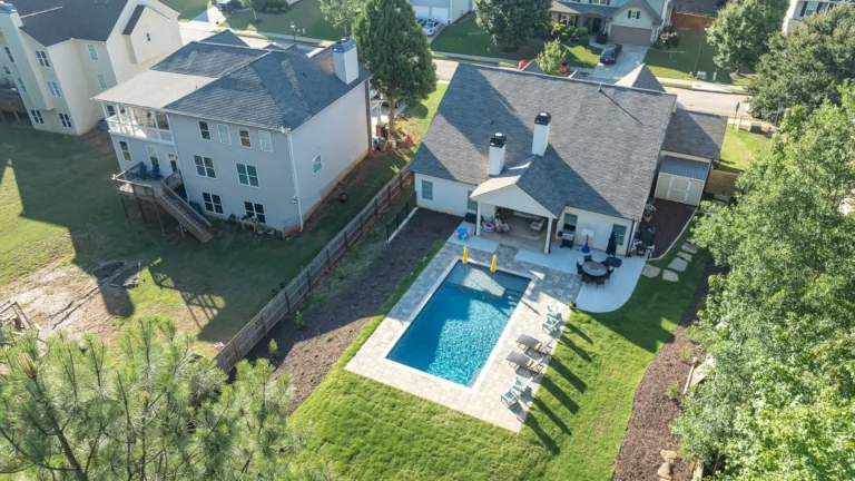 Aerial view of a backyard with a blue rectangular pool beside a house and patio, surrounded by green grass.