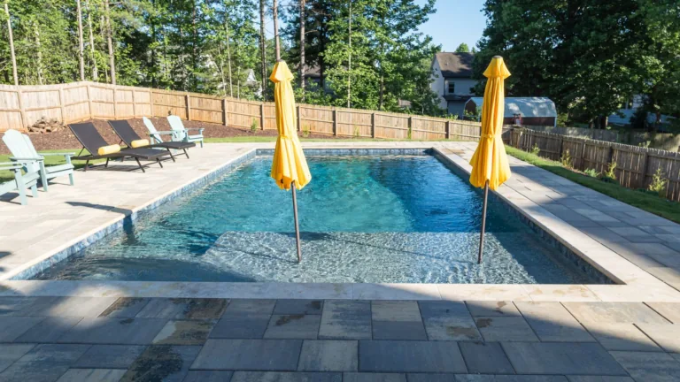 Outdoor swimming pool with two yellow umbrellas, lounge chairs, and trees in the background