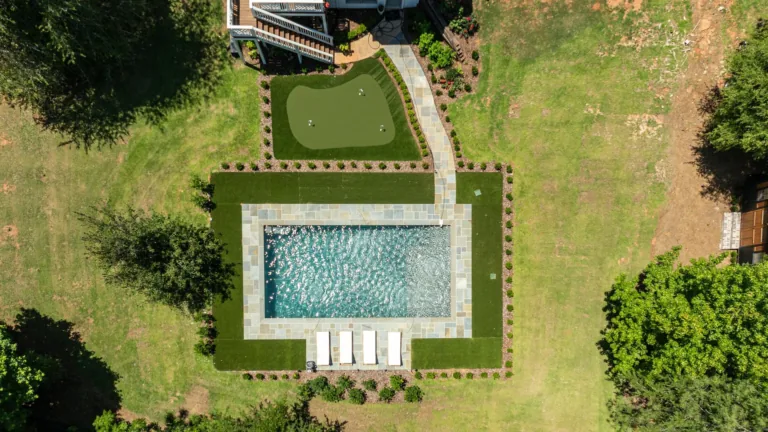 Aerial view of a backyard pool, patio loungers, and green lawn bordered by hedges