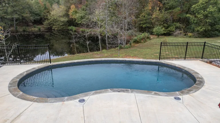 A large swimming pool is surrounded by trees and a fence.