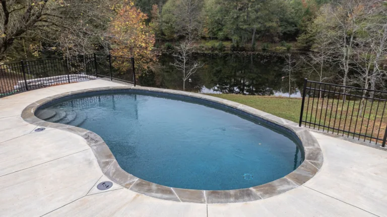 A large swimming pool is surrounded by a fence and trees.
