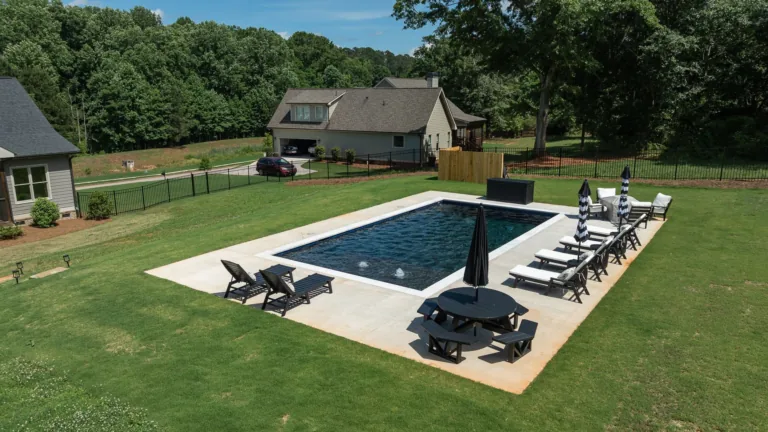 Backyard with rectangular swimming pool, lounge chairs, and a covered grill on a grassy lawn.
