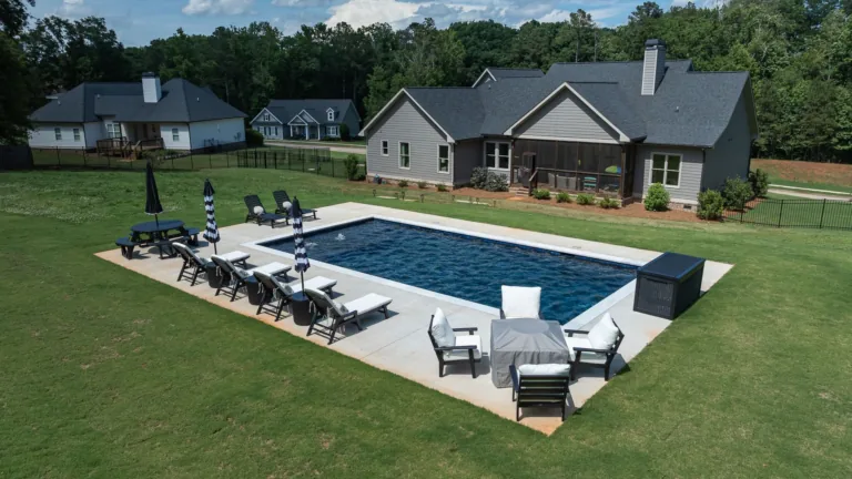 Backyard with a rectangular pool, lounge chairs, and a patio beside a large house