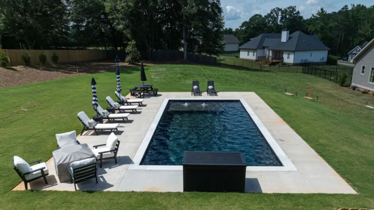 Backyard pool with lounge chairs, umbrellas, and a white deck in a grassy suburban yard.