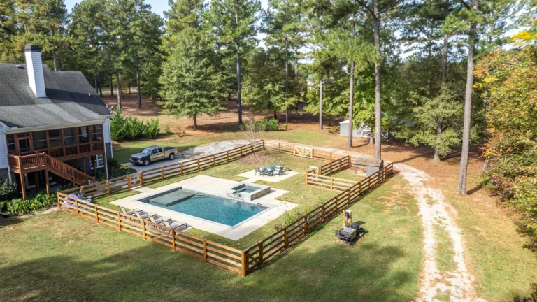 An aerial view of a house with a large swimming pool surrounded by trees.