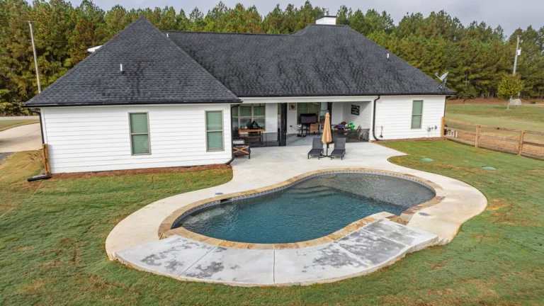 A white house with a large swimming pool in front of it.