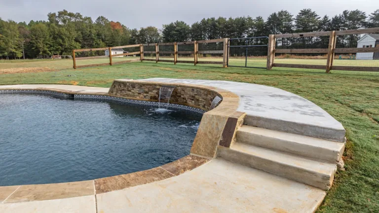 A swimming pool with stairs leading to it and a wooden fence in the background.