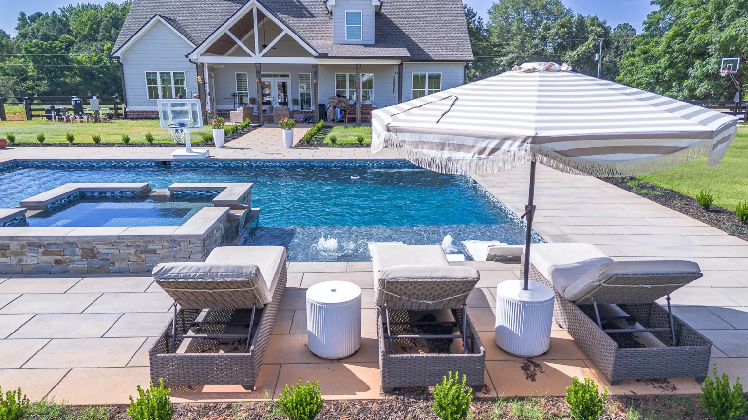 Poolside scene: Lounge chairs with umbrella, pool, and house in background.
