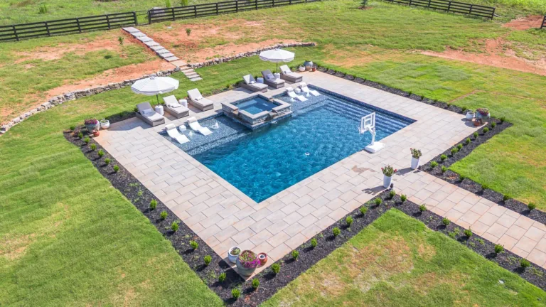 Aerial view of a backyard pool with lounge chairs, hot tub, and a grassy lawn.