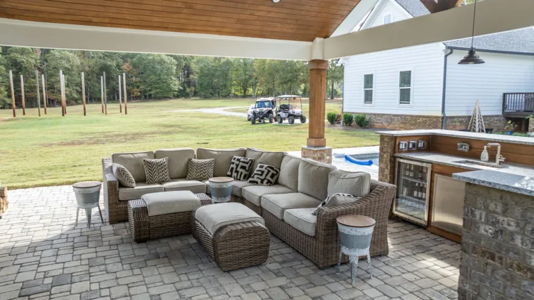 A patio with a couch , ottoman , table , and refrigerator.