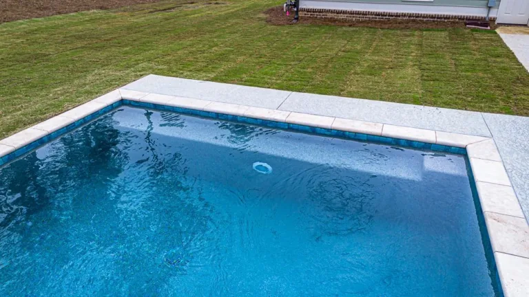 Blue swimming pool with white border and green grass in the background.