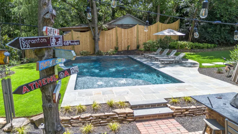 Backyard with pool, wooden fence, string lights, signs, and lounge chairs.