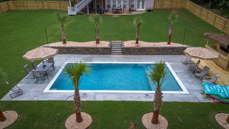 Backyard pool with palm trees, lounge area with umbrellas, and steps leading up to a grassy area.