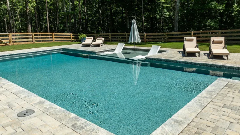 Backyard swimming pool with lounge chairs, umbrella, and a wooded fence line