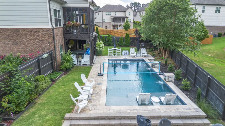 Backyard pool with lounge chairs, a screened porch, and a green lawn, surrounded by a black fence.