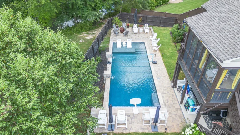 Aerial view of a rectangular swimming pool with lounge chairs, next to a house with a screened porch.