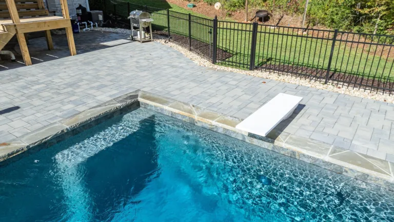 A large swimming pool is surrounded by a fence and a patio.