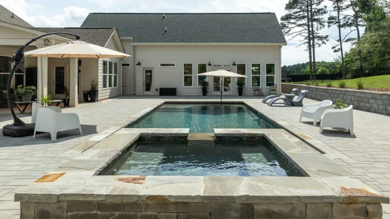 Modern backyard with a large pool, hot tub, lounge chairs, and a white house in the background