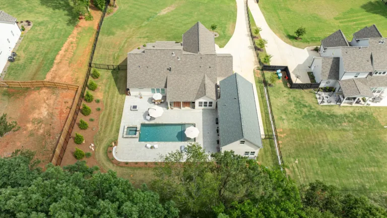 Aerial view of a suburban house with a backyard pool, patio, and surrounding lawn.