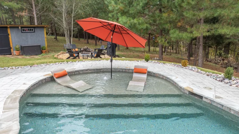 A swimming pool with a red umbrella and two lounge chairs in it.