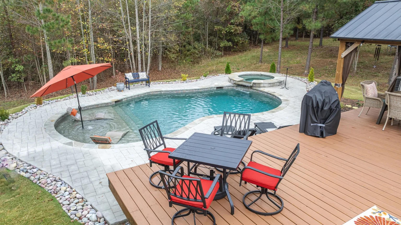 There is a table and chairs on the deck next to a pool.