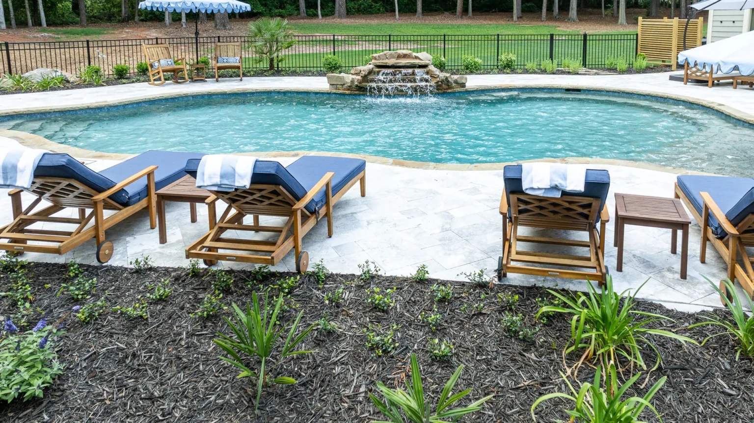 Backyard pool with wooden lounge chairs on a patio and landscaped garden border