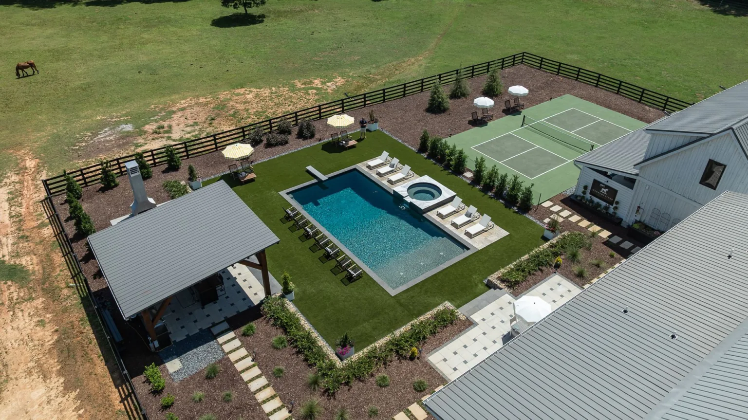 Aerial view of a backyard with pool, hot tub, tennis court, lounge chairs, and a covered patio.
