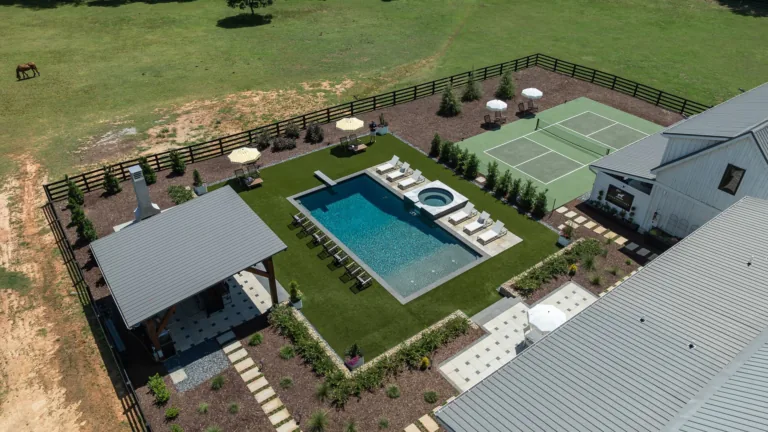 Aerial view of a backyard with pool, hot tub, tennis court, lounge chairs, and a covered patio.