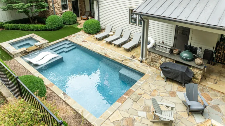 Backyard pool with stone patio, hot tub, lounge chairs, and covered grill area