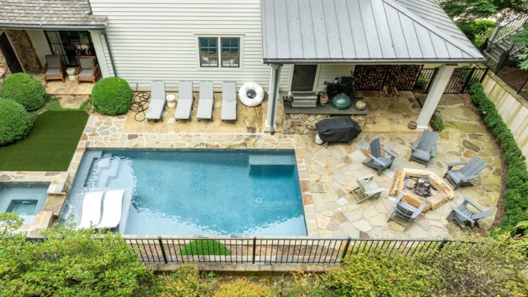 Backyard with a small blue pool, stone patio, lounge chairs, and covered seating area