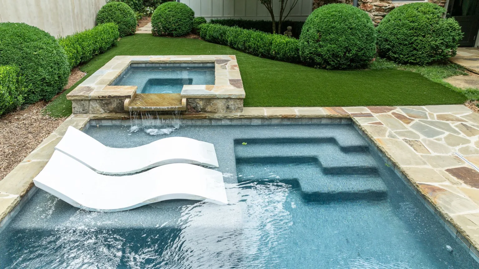 Backyard pool with stone deck, green lawn, and a white floating lounger in the water