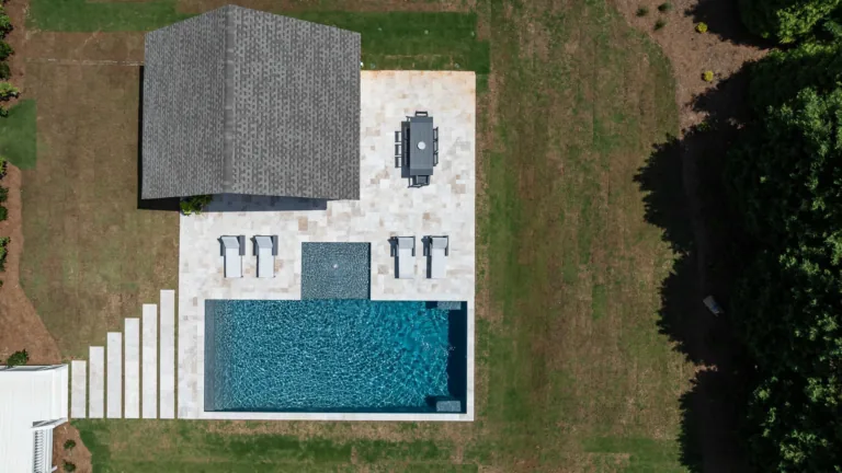 Aerial view of a backyard pool patio with lounge chairs, a hot tub, and a small covered structure.